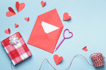 Love letter Valentine day concept. Red paper envelope with a white note inside and paper hearts a gift on a blue background.