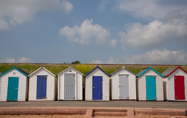 Fototapeta na wymiar Beautiful colourful beach huts by the beach with blue sky and clouds in the background