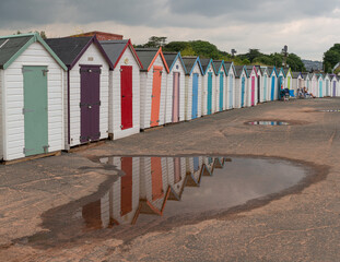 Naklejka premium Colourful wooden beach huts and reflection in puddle