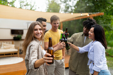 Cool diverse young friends toasting with beer bottles, drinking alcohol near camper van outdoors