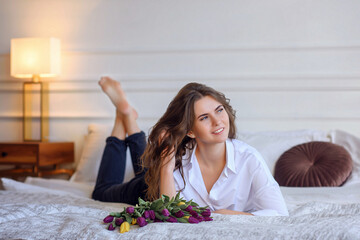 Obraz na płótnie Canvas beautiful sexy girl in jeans and a white shirt on a bed with flowers. March 8. Women's Day. mom's day
