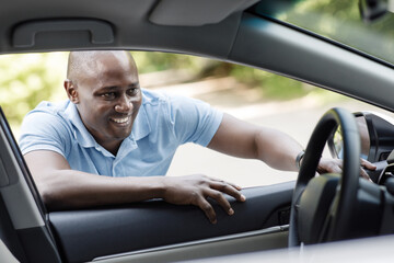 Happy african american man looking inside new car