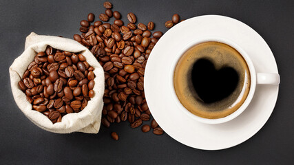 coffee cup with a heart sign and coffee beans in a sack on a dark background, top view.