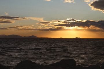 Tramonto con vista delle onde e di un'isola rocciosa. Punta ala