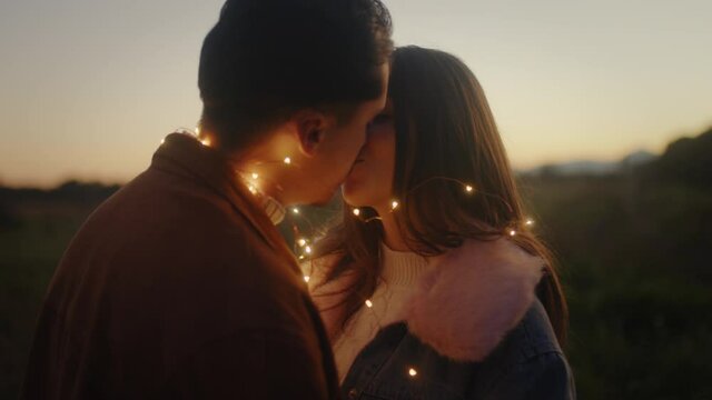 Giovane coppia di ragazzo e ragazza si bacia con striscia di luci led al tramonto