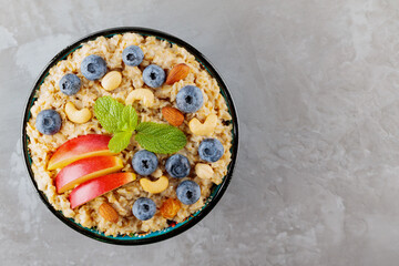 Oatmeal with blueberries, apple slices and nuts. Bowl of oatmeal porridge on gray background. Healthy eating, dieting, vegetarian food concept. Copy space. Top view