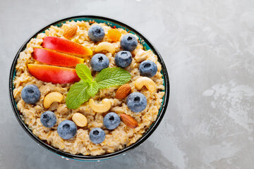 Oatmeal with blueberries, apple slices and nuts. Bowl of oatmeal porridge on gray background. Healthy eating, dieting, vegetarian food concept. Copy space. Top view