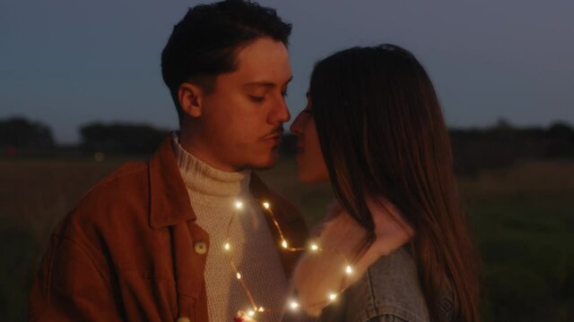 Giovane coppia di ragazzo e ragazza si bacia con striscia di luci led al tramonto