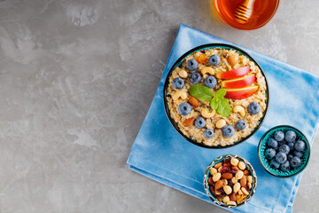 Cooked oatmeal, blueberries, nuts, apple slices and honey. Oatmeal and the ingredients for a healthy breakfast on a gray background. Top view. Copy space