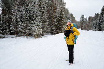 Fototapeta na wymiar A man walks through the woods with a hiking backpack. Panoramic view of landscape. Survival in the wild. Bright winter equipment Walking in the winter season