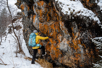 bush craft. The traveler climbing the mountain in winter. Snowy forest and rocks. Stick, cane for support. Survival in the wild.