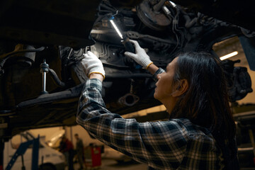 Focused woman checking mechanisms of a vehicle under lamp light