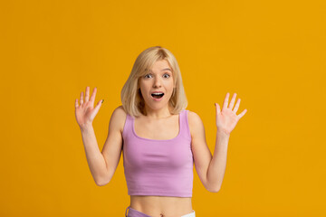 Portrait of overjoyed and surprised young lady looking at camera and spreading hands, isolated over yellow background