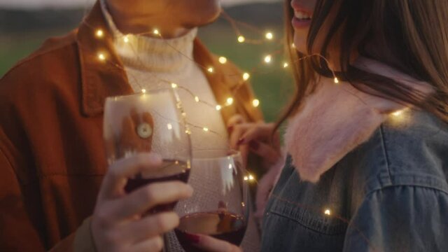 Giovane coppia al tramonto con calice di vino in mano e striscia di luci led bianche 