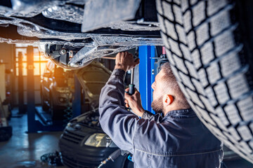 Mechanic repairs car chassis using a car lift. Auto service station background.