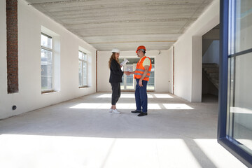 Pleased woman designer giving handshake to construction worker indoors