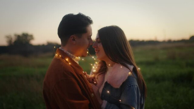 Giovane coppia di ragazzo e ragazza si bacia con striscia di luci led al tramonto