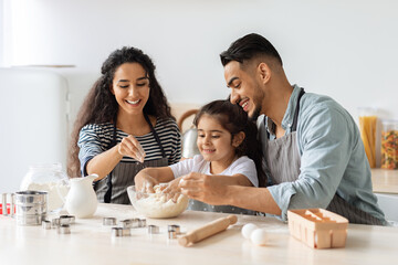 Cheerful arab parents making cookies with their little daughter