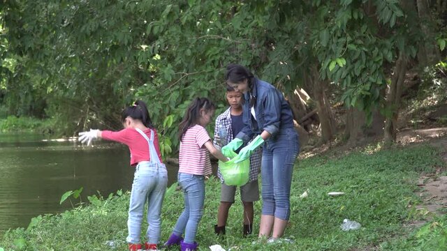Group of asian kids and teacher school volunteer charity environment under tree near river water. volunteer charity to green recycling bag cleaning park together at ratchaburi thailand.