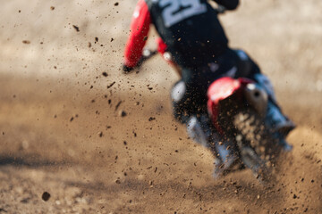 Motocross rider creates a huge cloud of dust and stone, flying debris from a motocross in dirt track