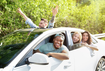 Joyful young multiracial friends going on road trip by car, looking through windows, having...