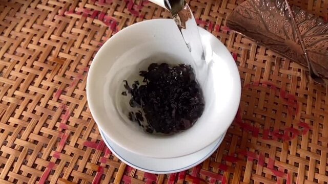 brew Chinese oolong tea. Hot water is rushed down from a height and the particles of Tieguanyin tea leaves swirl around in water, forming a whirlpool. White tea set in a tea bowl.Slow motion.