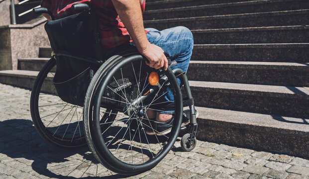 Young man with a physical disability who uses wheelchair in front of the stairs