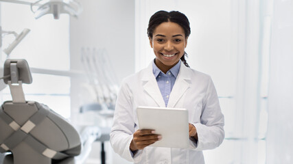 Portrait of happy black female dentist in white coat with digital tablet