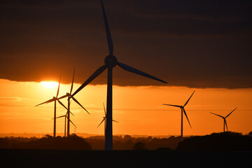 Deep orange sunset falls behind a field of giant wind turbines