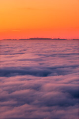 Fototapeta na wymiar The French and Italian Alps silhouetted against an orange sky above a cloud inversion viewed from Corsica at sunset