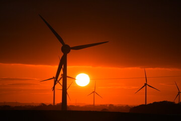 Deep orange sunset falls behind a field of giant wind turbines