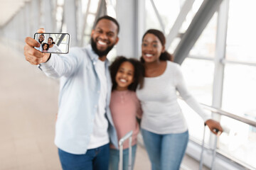 Black family of three traveling, taking selfie in modern airport