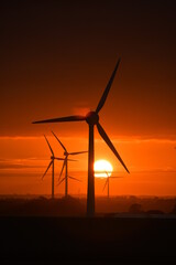 Deep orange sunset falls behind a field of giant wind turbines