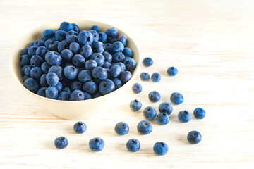 Fresh ripe organic blueberries in bowl on white wooden background with copy space for text