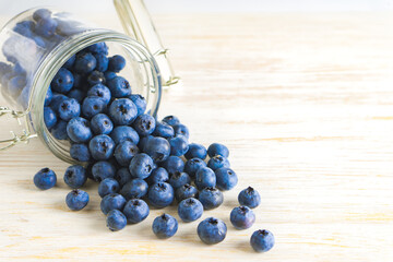 Fresh organic blueberries are scattered from glass jar on white wooden table. close-up photo with copy space for text