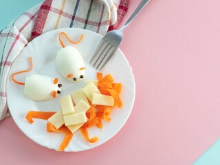 Food for a children's party. Boiled egg mice with carrot ears and tail, cheese and carrot slices in a white plate on a pink background, metal fork. Creative food design. Place of text.