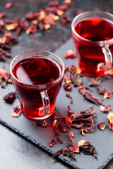 Hibiscus tea in glass mug on a dark background. Cup of red hibiscus tea and dry hibiscus petals on a slate board © Lazartivan