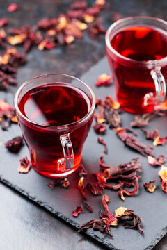 Hibiscus tea in glass mug on a dark background. Cup of red hibiscus tea and dry hibiscus petals on a slate board