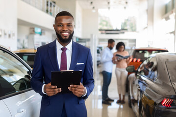 Handsome Black Car Salesman In Suit Posing At Workplace In Auto Showroom