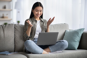 Naklejka premium Pretty young asian lady sitting on couch with laptop