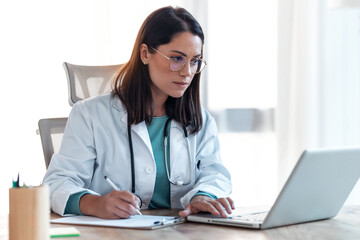 Attractive female doctor working with her computer in medical consultation.