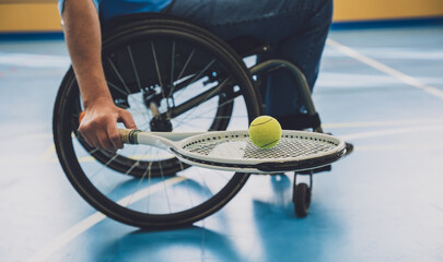 Adult man with a physical disability who uses wheelchair playing tennis on indoor tennis court