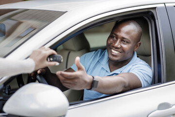 Black man taking key from car, renting auto for trip