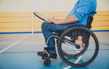 Adult man with a physical disability who uses wheelchair playing tennis on indoor tennis court