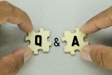 fingers holding a wooden puzzle with the letters Q and A. question and answer concept