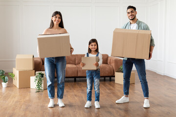 Fototapeta na wymiar Happy young family of three holding boxes in new flat