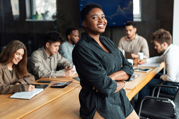 Smiling African American businesswoman sitting on desk and posing