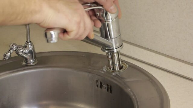 Old faucet with soft pipes takedown from gray stainless steel kitcken sink hole on white kitchen table with plumber white hands