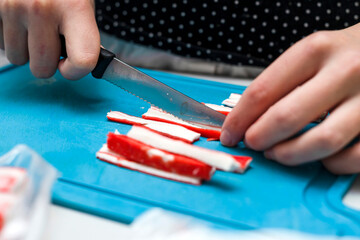 The girl cuts crab sticks into slices, preparation for making sushi.