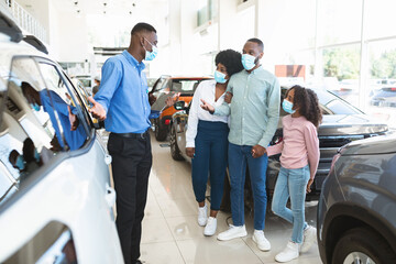 Black family speaking to car salesman, purchasing new auto during coronavirus lockdown at...